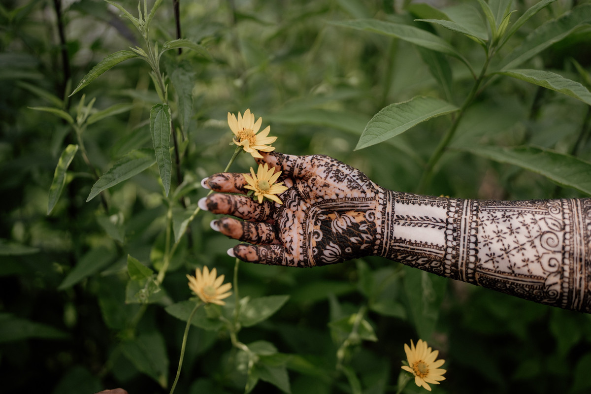 Hennaed hand reaching toward yellow wildflowers among green leaves